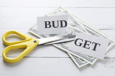 Photo of Cut paper with word Budget, dollar banknotes and scissors on white wooden table