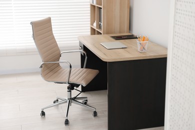 Beige leather chair, laptop and desk in office