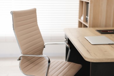 Photo of Beige leather chair, laptop and desk in office, closeup