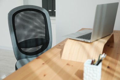 Photo of Grey chair, laptop and desk in office, closeup