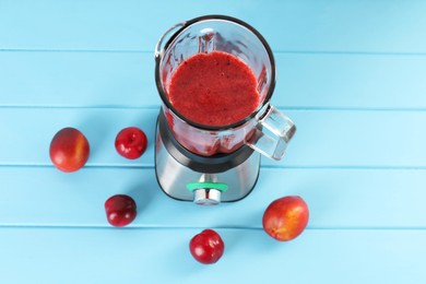 Blender with mixture of ingredients and fresh fruits on light blue wooden table, above view