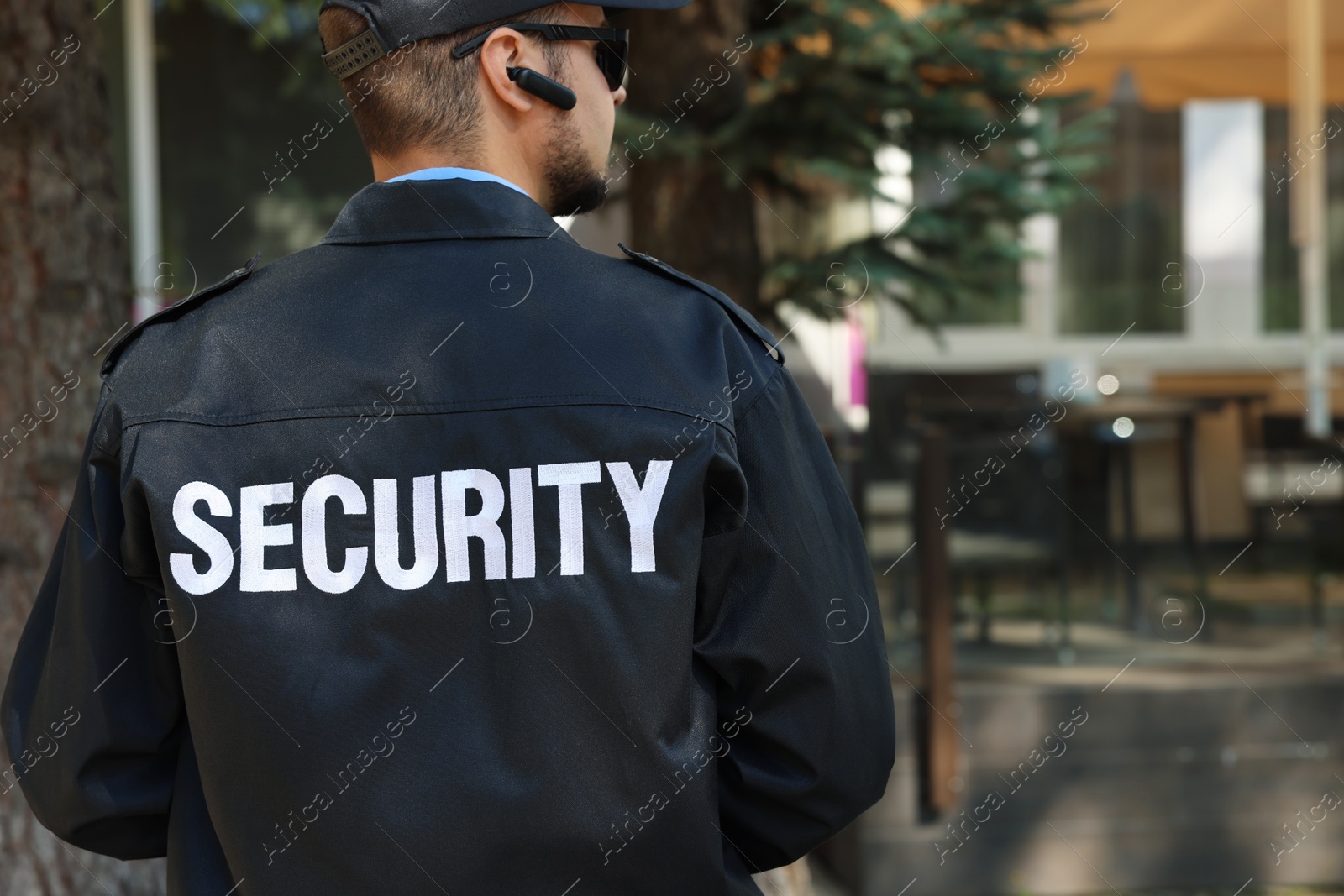 Photo of Security guard in uniform and sunglasses outdoors, back view