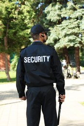 Photo of Security guard in uniform with baton outdoors, back view