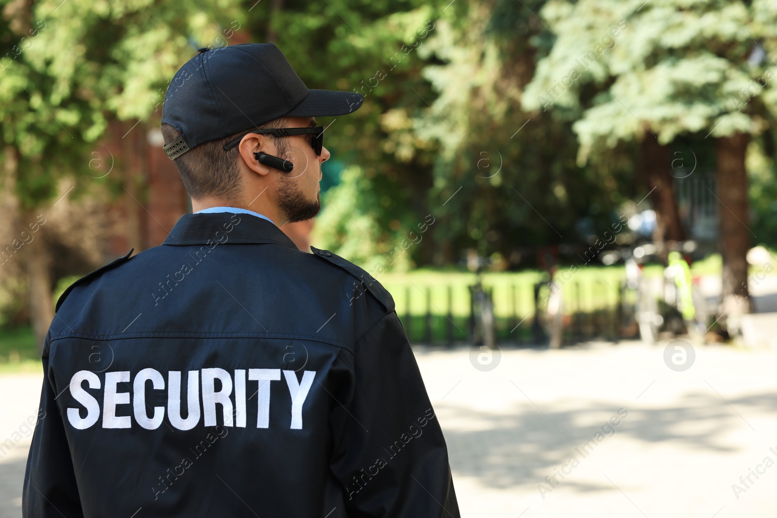 Photo of Security guard in uniform and sunglasses outdoors, back view. Space for text