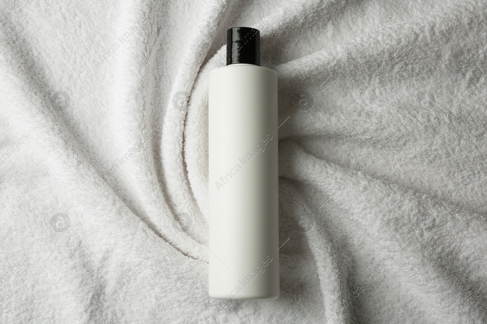 Photo of Bottle of shampoo on soft terry towel, top view