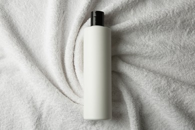 Photo of Bottle of shampoo on soft terry towel, top view