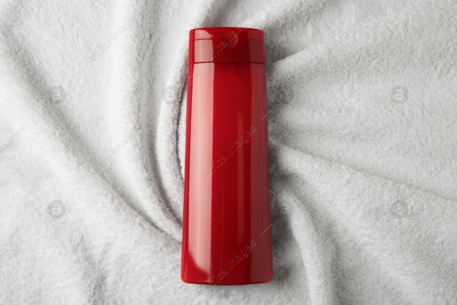 Photo of Bottle of shampoo on soft terry towel, top view