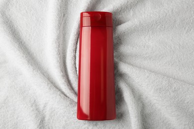 Photo of Bottle of shampoo on soft terry towel, top view