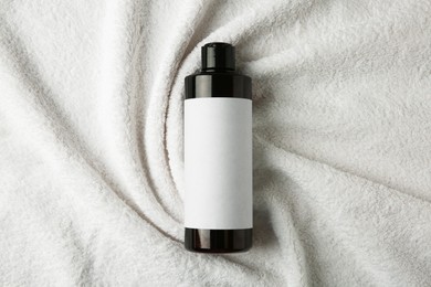 Photo of Bottle of shampoo on soft terry towel, top view