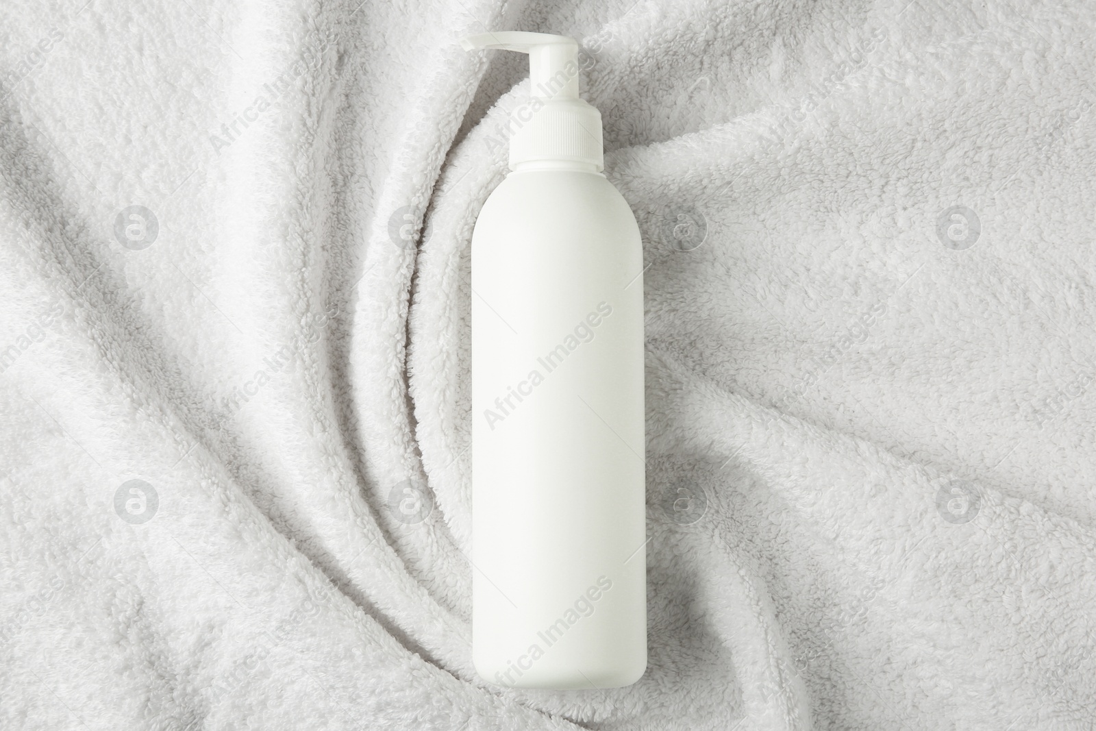 Photo of Bottle of shampoo on soft terry towel, top view