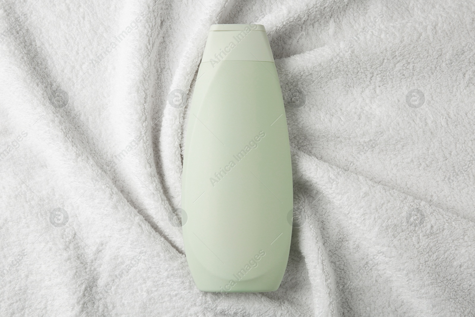 Photo of Bottle of shampoo on soft terry towel, top view