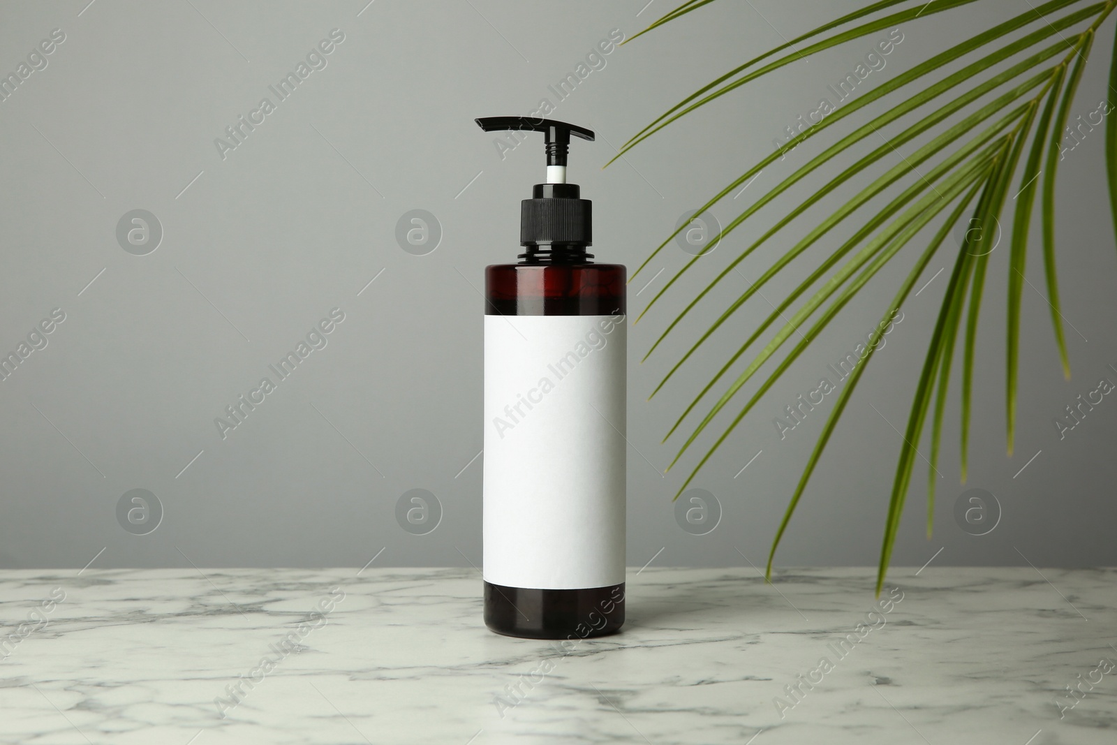 Photo of Bottle of shampoo on white marble table against grey background