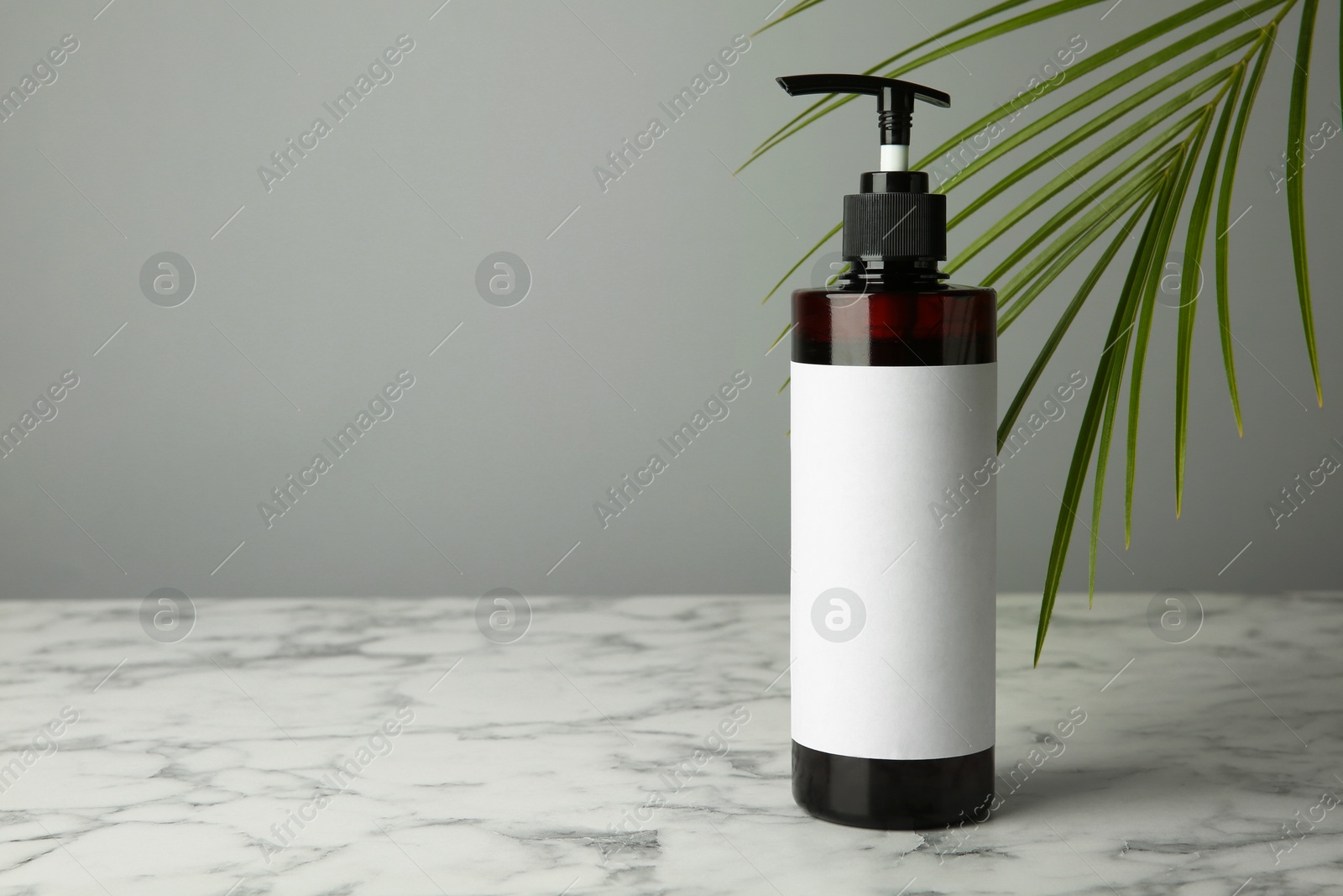 Photo of Bottle of shampoo on white marble table against grey background. Space for text