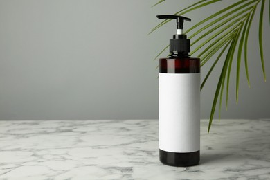 Photo of Bottle of shampoo on white marble table against grey background. Space for text