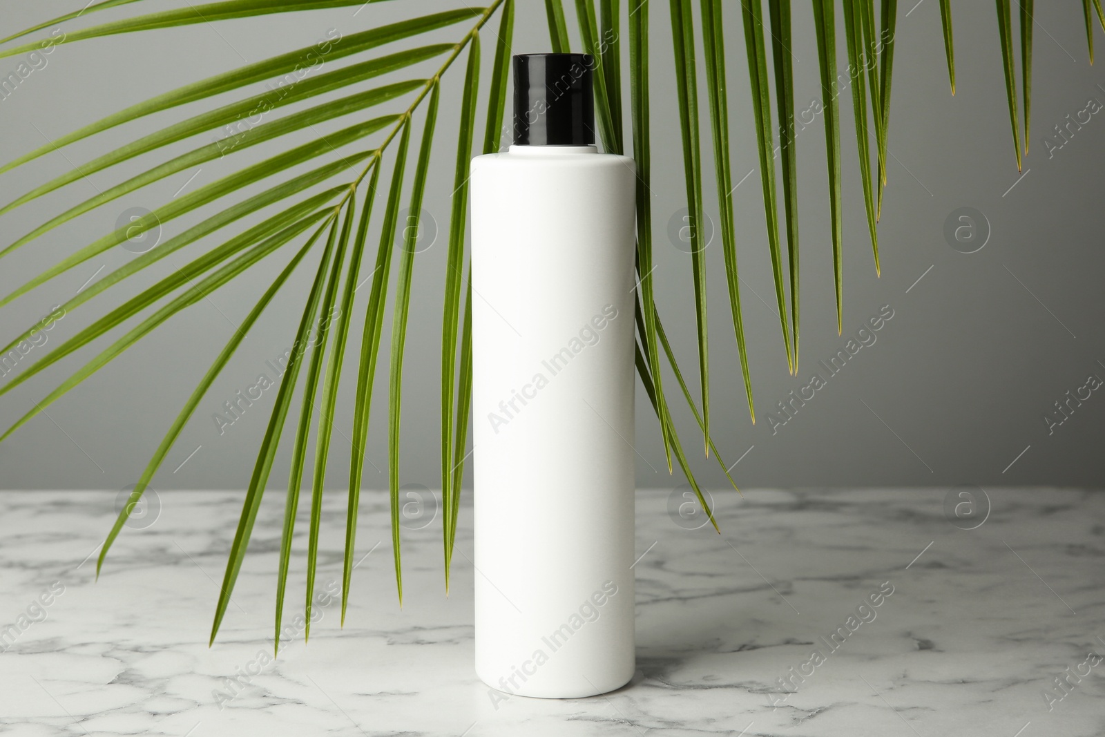 Photo of Bottle of shampoo on white marble table against grey background