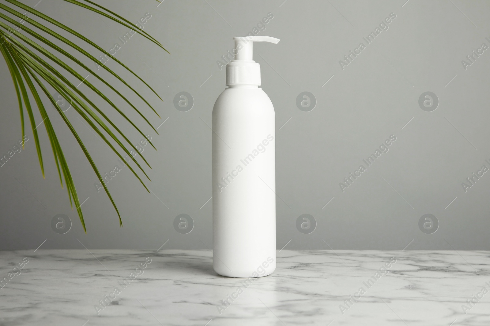 Photo of Bottle of shampoo on white marble table against grey background