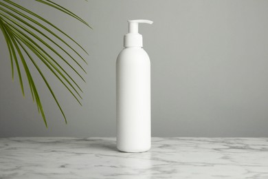 Photo of Bottle of shampoo on white marble table against grey background