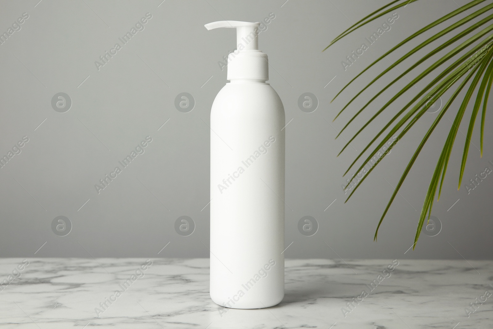 Photo of Bottle of shampoo on white marble table against grey background