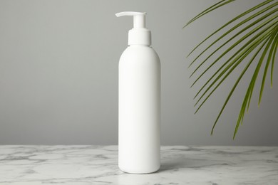 Photo of Bottle of shampoo on white marble table against grey background