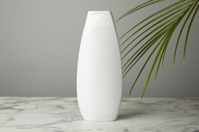 Photo of Bottle of shampoo on white marble table against grey background