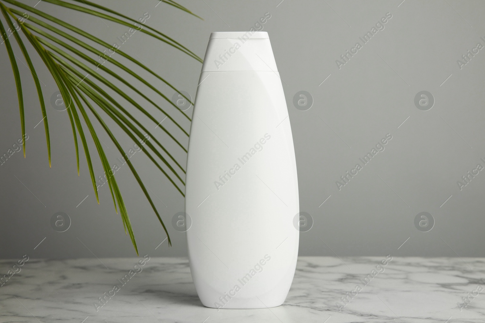 Photo of Bottle of shampoo on white marble table against grey background