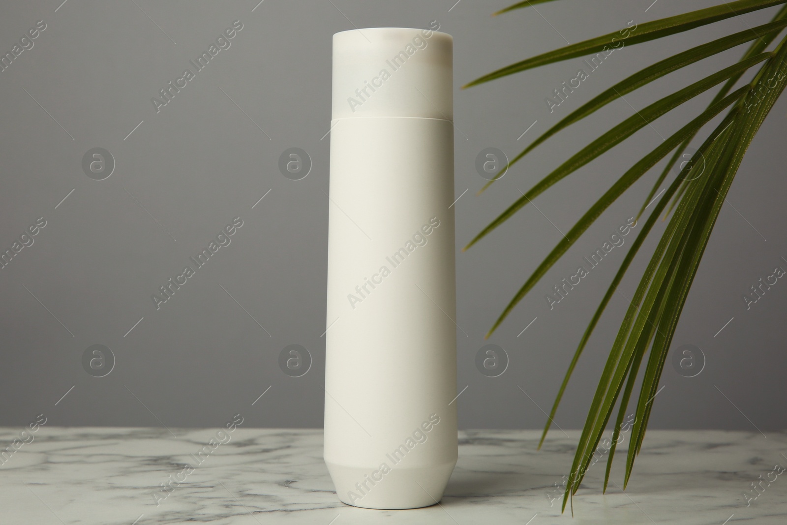 Photo of Bottle of shampoo on white marble table against grey background