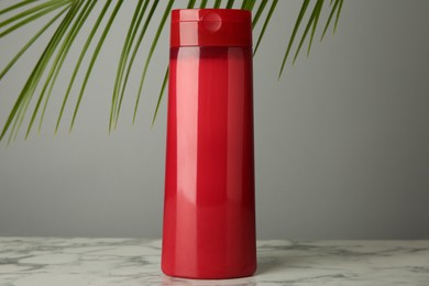 Photo of Bottle of shampoo on white marble table against grey background