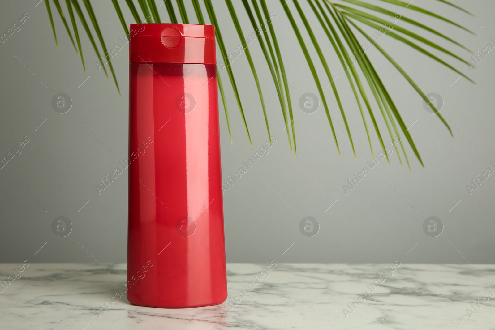 Photo of Bottle of shampoo on white marble table against grey background. Space for text