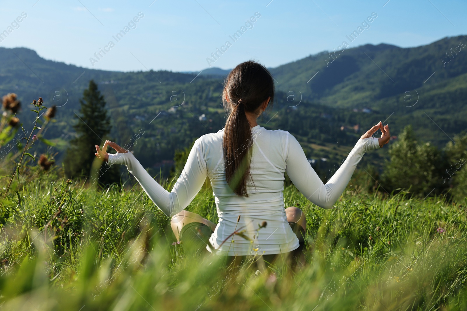 Photo of Woman on green grass in beautiful mountains, back view