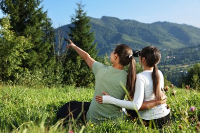 Women with binoculars on green grass in beautiful mountains, back view