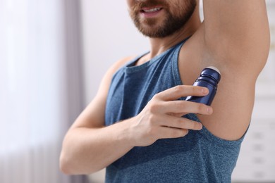 Photo of Smiling man applying roll-on deodorant at home, closeup