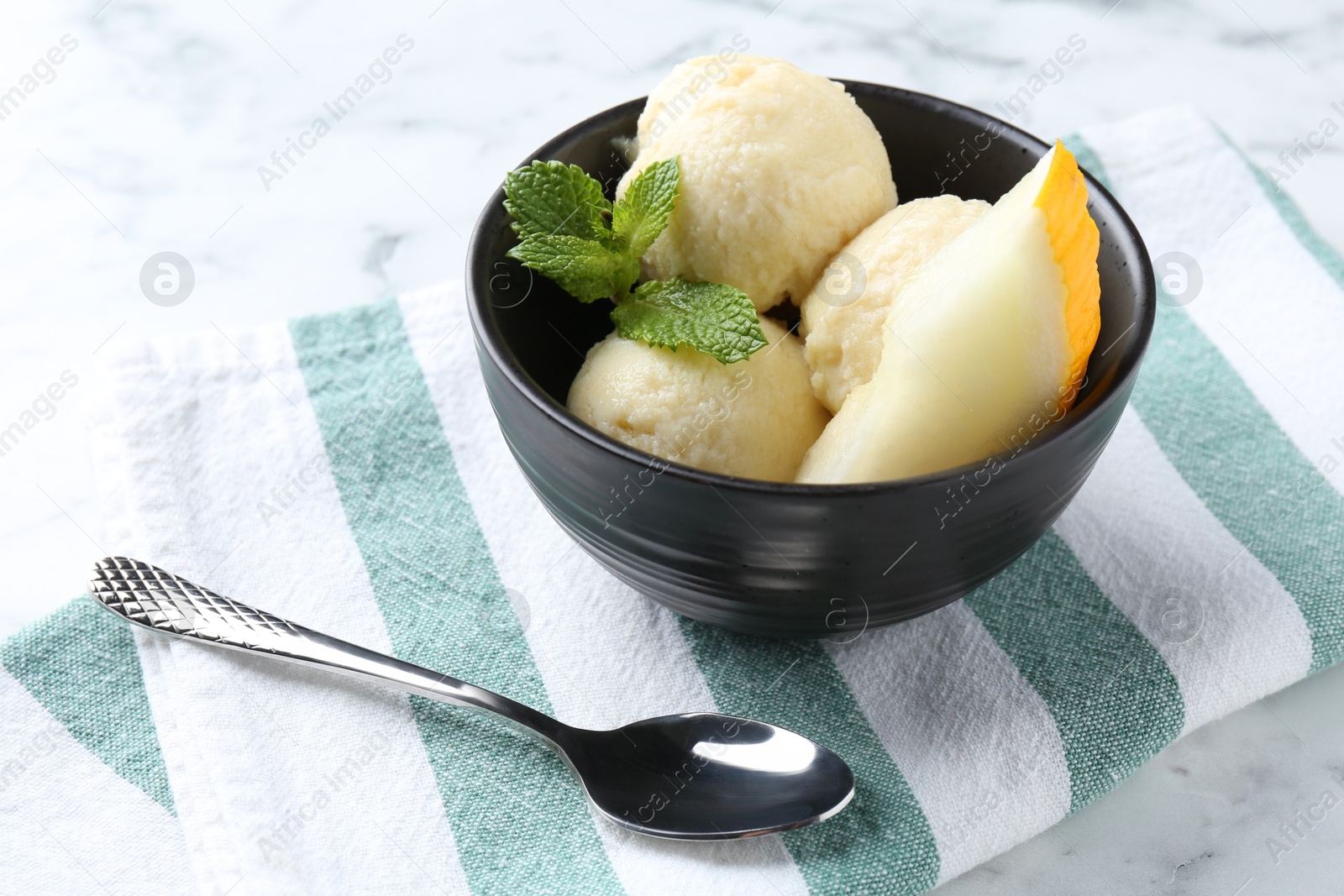 Photo of Scoops of tasty melon sorbet with mint in bowl and spoon on white table