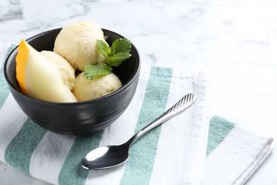 Photo of Scoops of tasty melon sorbet with mint in bowl and spoon on white marble table, space for text