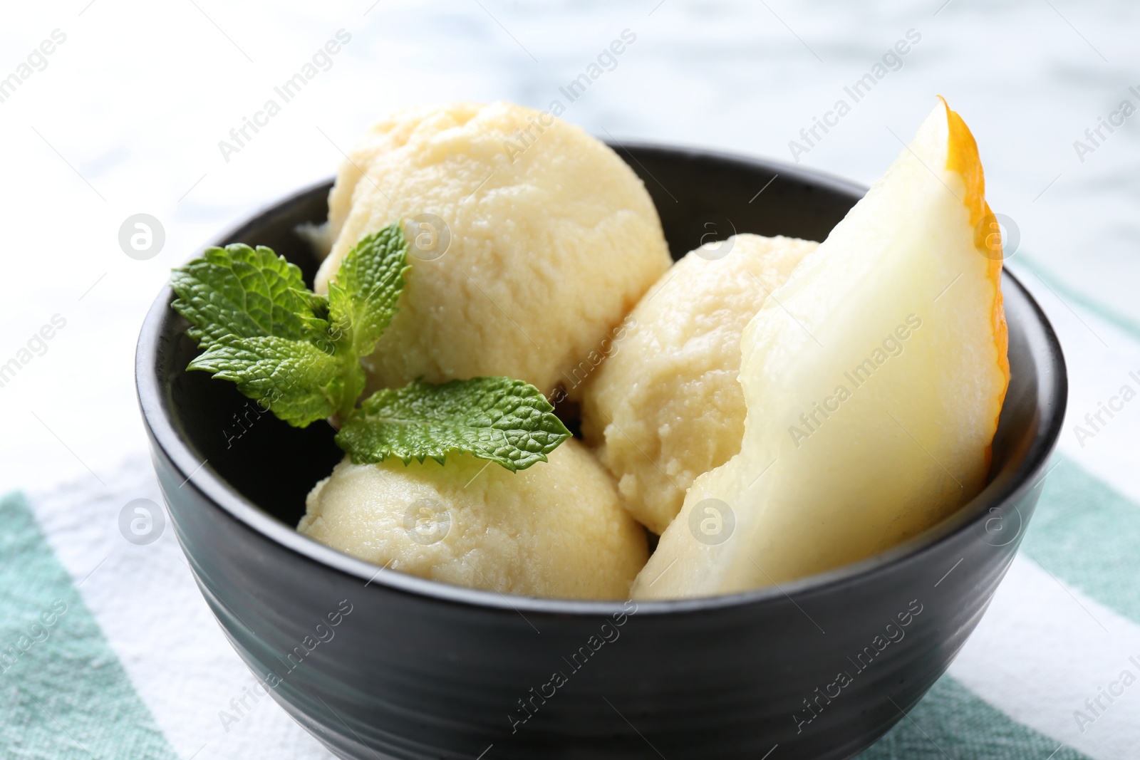 Photo of Scoops of tasty melon sorbet with mint and fresh fruit in bowl on white table, closeup