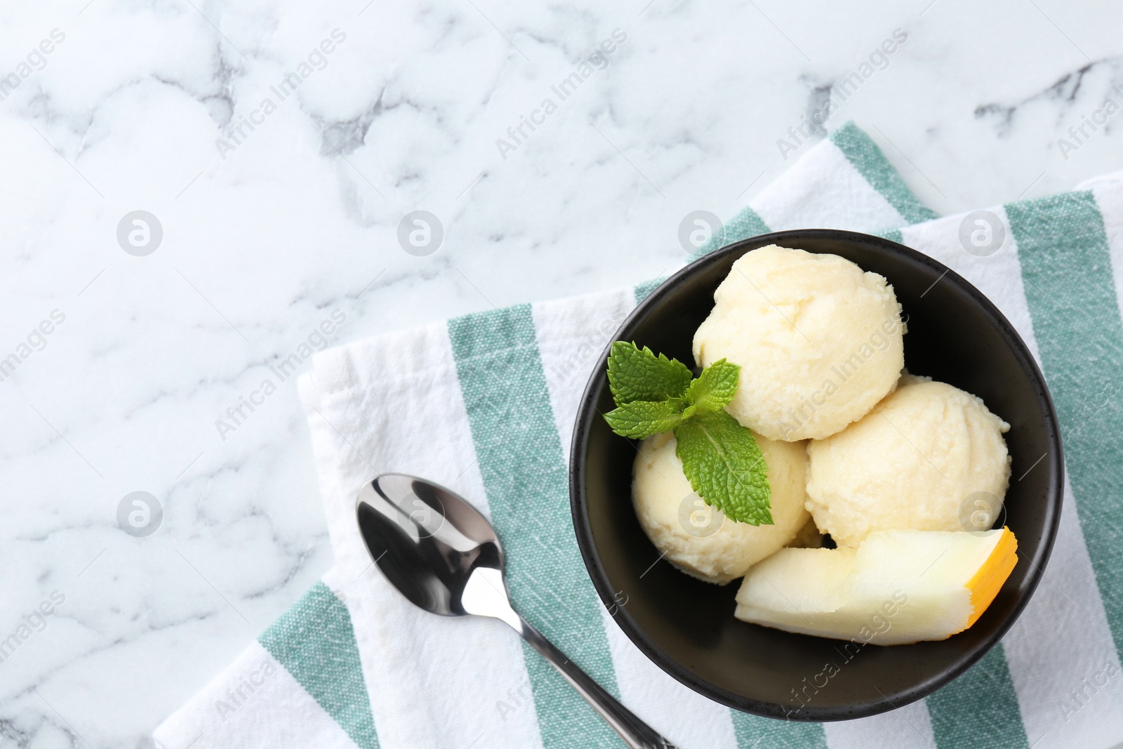 Photo of Scoops of tasty melon sorbet with mint in bowl and spoon on white marble table, flat lay. Space for text