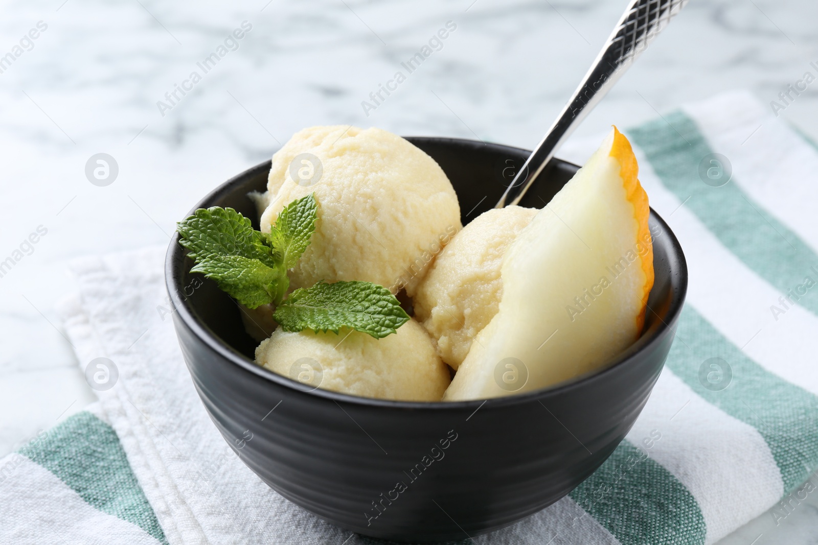 Photo of Scoops of tasty melon sorbet with mint and spoon in on white table, closeup