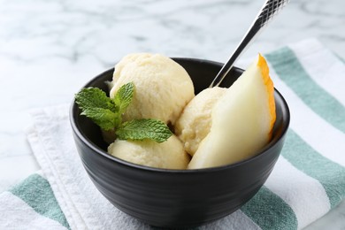 Photo of Scoops of tasty melon sorbet with mint and spoon in on white table, closeup