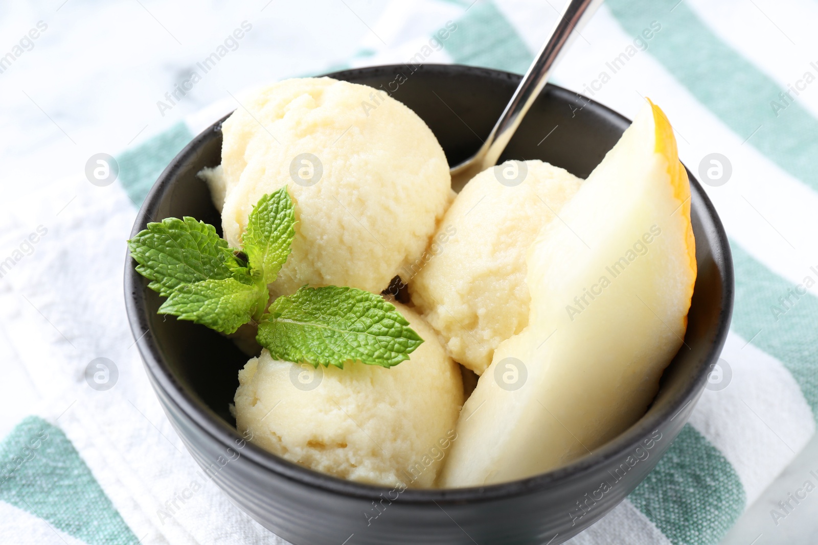 Photo of Scoops of tasty melon sorbet with mint and spoon in on white table, closeup