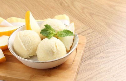 Photo of Scoops of tasty melon sorbet with mint in bowl and fresh fruit on wooden table, space for text