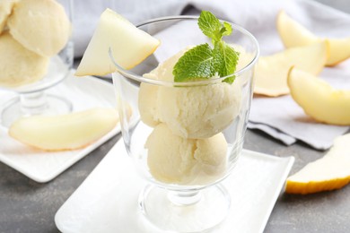 Photo of Scoops of melon sorbet with mint and fresh fruit in glass dessert bowl on grey table, closeup