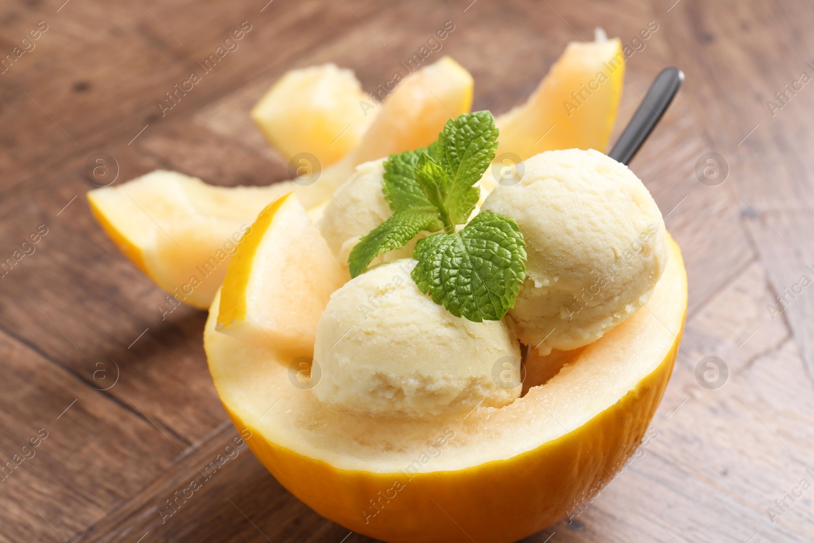 Photo of Scoops of tasty melon sorbet with mint in fresh fruit on wooden table, closeup