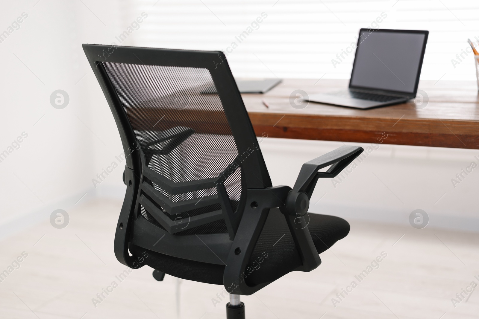 Photo of Black chair, laptop and desk in office, closeup