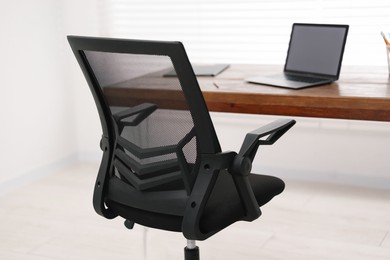 Photo of Black chair, laptop and desk in office, closeup