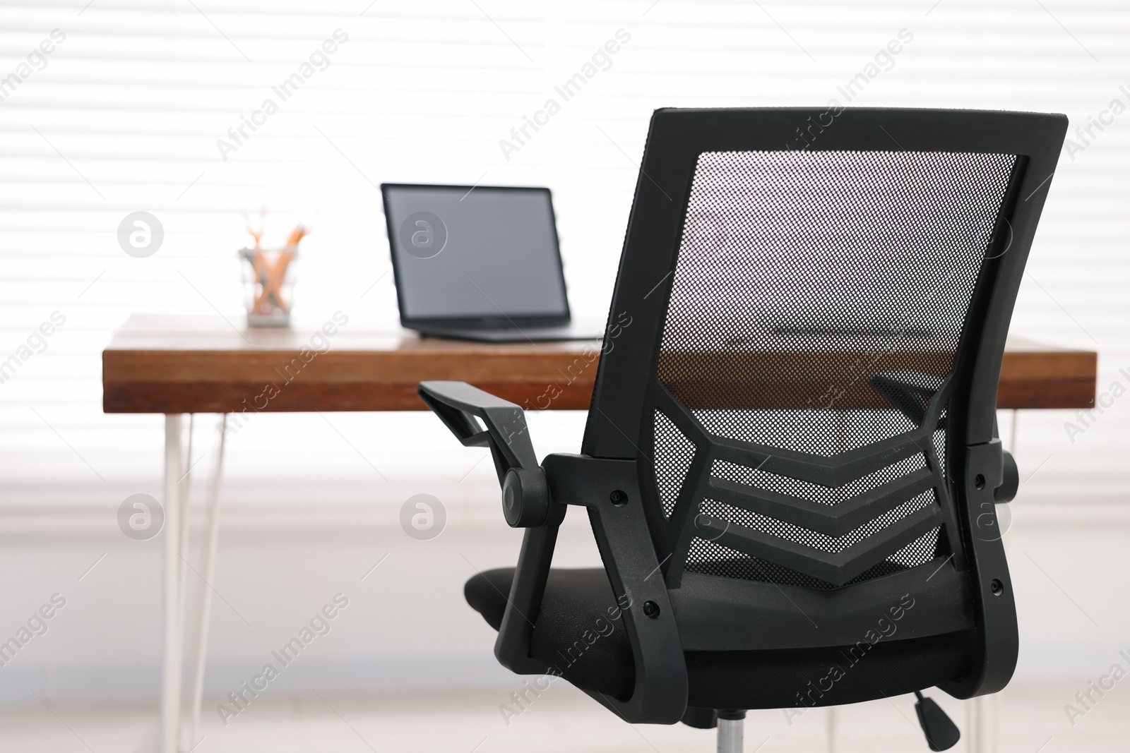 Photo of Black chair, laptop and desk in office, closeup