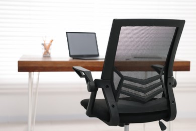 Black chair, laptop and desk in office, closeup