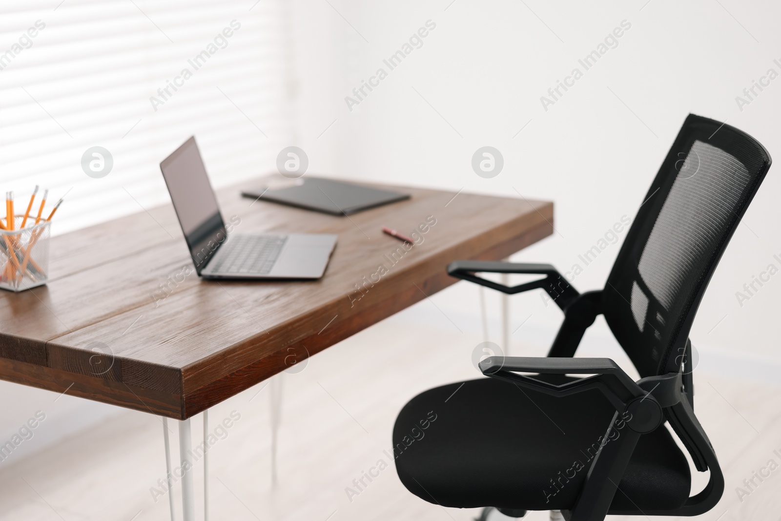 Photo of Black chair, laptop and desk in office, closeup