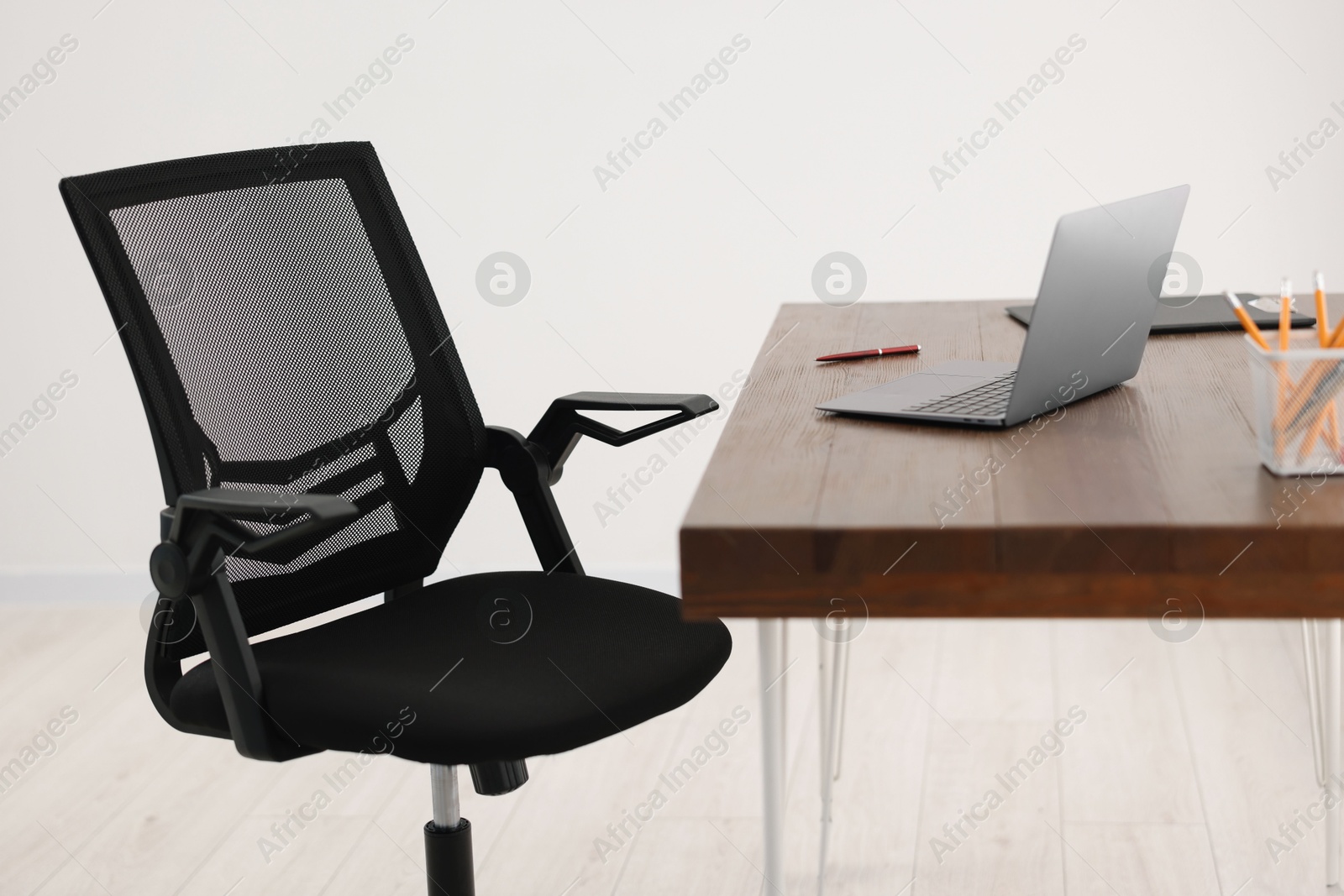 Photo of Black chair, laptop and desk in office, closeup