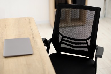 Photo of Black chair, laptop and desk in office, closeup