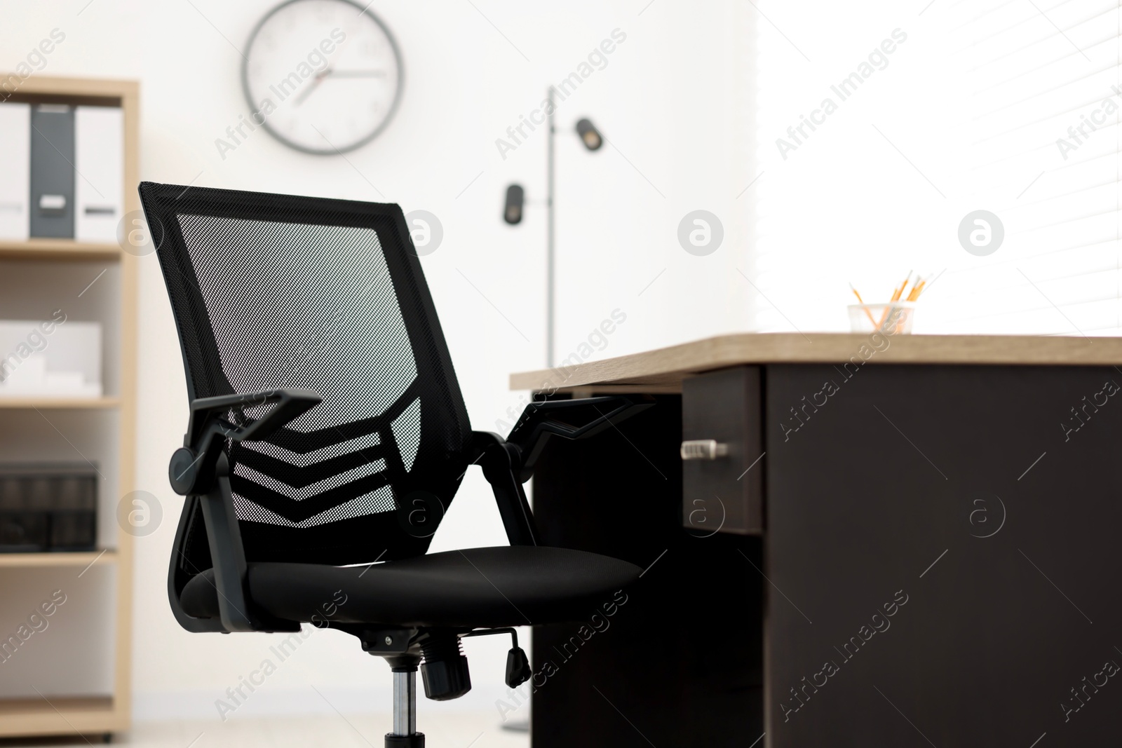 Photo of Black chair and wooden desk in office, closeup