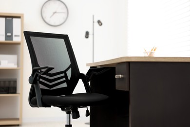 Photo of Black chair and wooden desk in office, closeup